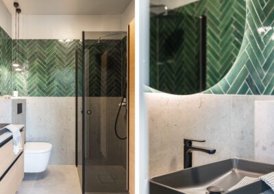 Ett elegant badrum med en vägg av grönt fiskbensmönstrat kakel, en minimalistisk toalett, och en mörk handfat med en svart kran.
