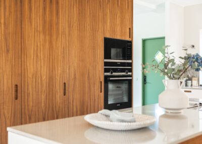 Kök med träskåp och inbyggda Siemens ugnar, mot en bakgrund av en grön dörr och en vas med eukalyptus.
