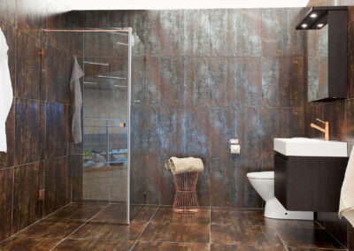 Ett badrum med rostliknande kakel på väggarna och golvet som skapar en unik, industriell känsla. En glasvägg skiljer duschområdet och resten av badrummet.