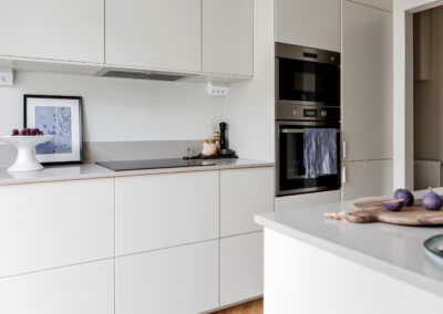 Ett fräscht och minimalistiskt kök med släta vita skåp, grå bänkskivor och moderna inbyggda ugnar, designat för enkelhet och elegans.