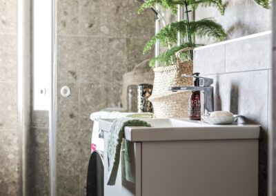 Badrum med grå marmorkakel, en modern handfat med tvål och handduk, och en korg med gröna växter som skapar en fridfull atmosfär.