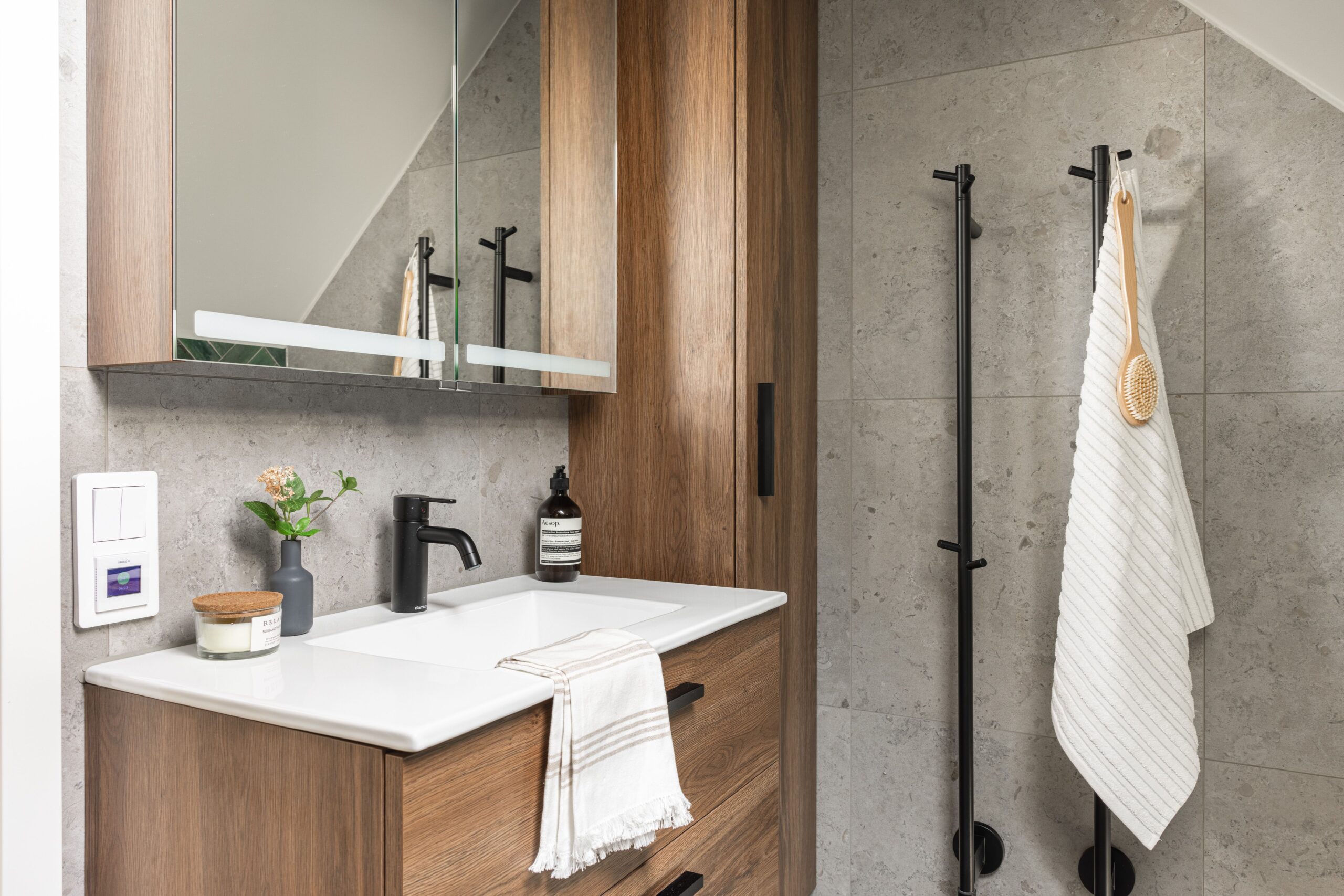 Ett modernt badrum med träskåp, en integrerad vit handfat, svarta kranar och en spegel.